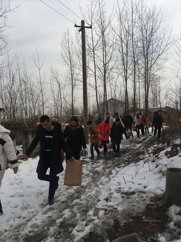 商會愛心慰問團團友正帶著尉問物品，踏著泥雪，迎著寒風，步入村道、前往慰問家庭